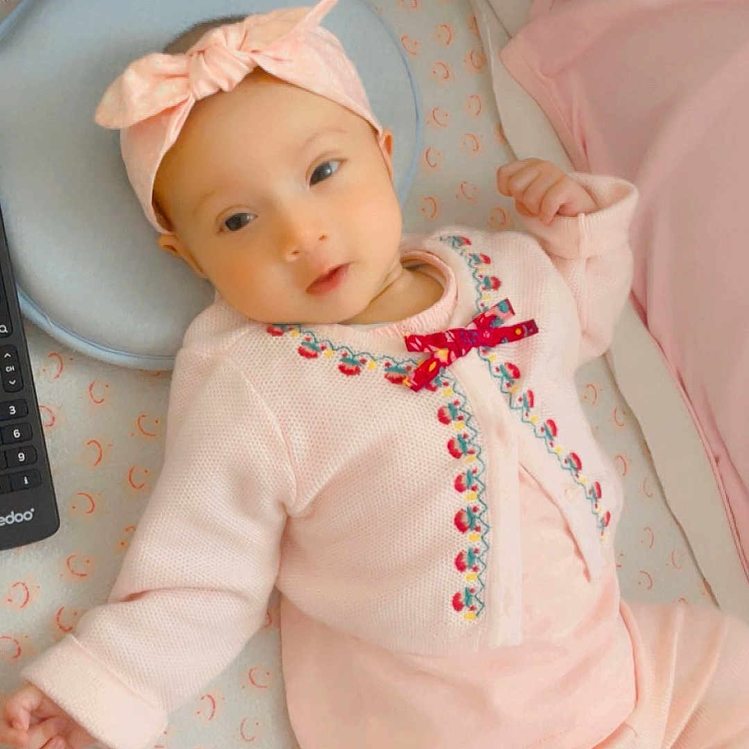 Emaan Ahsan Nabi a rejoint le concours — aidez-le/la à gagner de superbes lots ! baby, blanket, bow, child, cozy, crib, cute, headband, indoor, infant, lying_down, newborn, patterned_sheet, person, pink_clothing, portrait, remote_control, resting, sleepy, soft_lighting