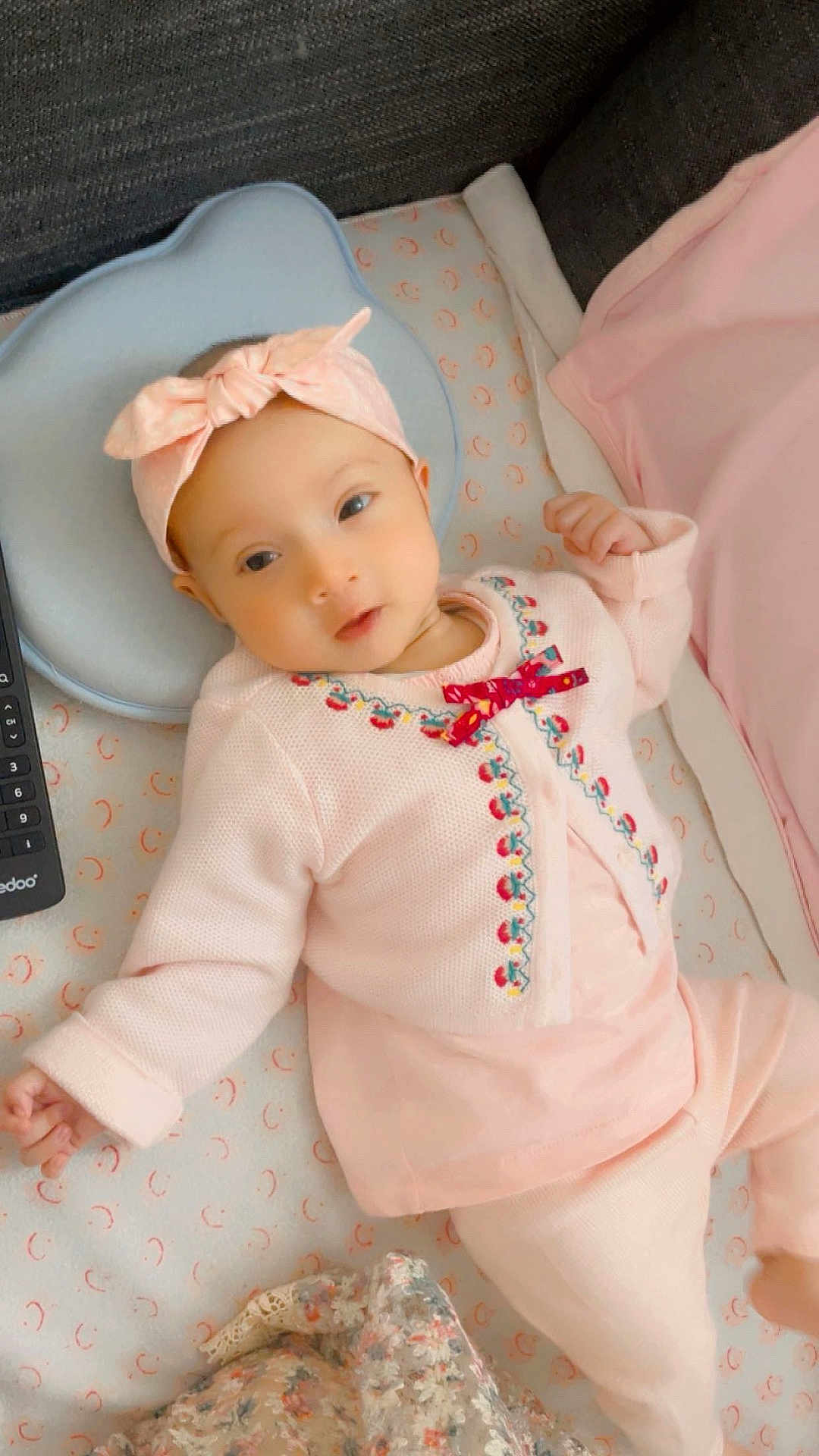 Emaan Ahsan Nabi a rejoint le concours — aidez-le/la à gagner de superbes lots ! baby, infant, pink_clothing, headband, bow, crib, blanket, remote_control, patterned_sheet, lying_down, cute, soft_lighting, indoor, child, sleepy, cozy, portrait, person, newborn, resting