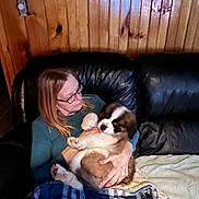 Tracy Pedder joined the competition — help win amazing prizes! woman, puppy, dog, saint_bernard, couch, leather, blanket, glasses, wood_paneling, indoor, pet, holding, seated, comfort, casual_clothing, relaxation, cozy, fur, cute, love