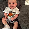 Landen is registered to the contest to win money with this photo: baby, smiling, child, turtle, tshirt, shorts, white_shoes, couch, indoor, happy, sitting, person, cute, infant, clothing, footwear, young_child, portrait, home, cozy