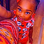 child, girl, smiling, braided_hair, beads, colorful_clothing, minnie_mouse, red_shirt, orange_pants, wooden_floor, indoors, selfie, cute, happy, portrait, person, bright_colors, patterned_fabric, hand, feet