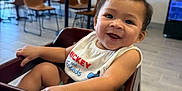 Tyson joined the competition — help win amazing prizes! baby, high_chair, smile, bib, indoor, child, wooden_furniture, table, restaurant, happy, person, clothing, seat, floor, face, hair, arm, hand, background, window