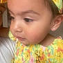 Oakley is registered to the contest to win money with this photo: child, toddler, face, earring, dress, colorful_clothing, yellow, cartoon_print, close_up, soft_focus, portrait, skin, hair, ear, person, indoor, cute, young_child, expression, curious
