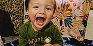 Harley joined the competition — help win amazing prizes! toddler, child, smiling, laughing, toy, green_shirt, red_shorts, blanket, floral_pattern, leopard_print, indoor, happy, cute, sitting, playful, person, face, head, legs, colorful
