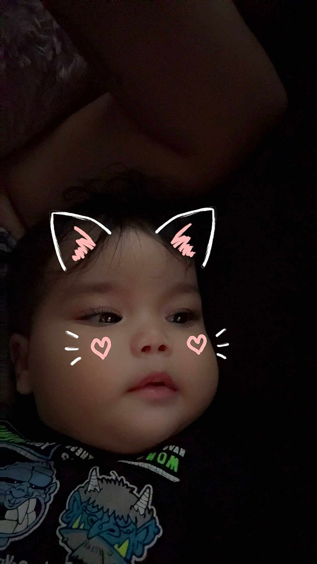 Charlotte is registered to the contest to win money with this photo: baby, child, face, cat_ears_filter, digital_filter, heart_cheeks, dark_background, cartoon_print, clothing, cute, portrait, indoors, young_child, expressionless, whiskers, head, closeup, soft_light, casual, person