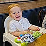 toddler, child, high_chair, toy, smiling, indoor, table, wood, white_clothing, red_hair, happy, person, playful, seat, furniture, cute, face, young_child, casual, baby