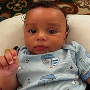 Hendrix joined the competition — help win amazing prizes! baby, infant, face, closeup, cute, blue_clothing, patterned_clothing, hand, eyes, curly_hair, cushion, carpet, indoors, portrait, child, young, skin, expression, person, soft_lighting