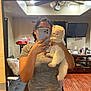 person, cat, mirror, indoor, selfie, phone, furniture, ceiling_fan, television, curtain, wood_floor, gray_shirt, black_pants, fluffy_cat, holding, reflection, home, living_room, cozy, cute