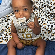 Jayceon is registered to the contest to win money with this photo: baby, infant, pacifier, clothing, champion, sporty, sitting, blanket, leopard_print, bed, white_shoes, curious, cute, indoors, person, child, footwear, sock, portrait, young