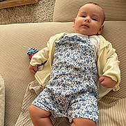 Leila participe au concours pour gagner de l'argent avec cette photo : baby, infant, child, couch, sofa, clothing, romper, cardigan, toy, striped_toy, plush_toy, beige, fabric, texture, indoor, person, relaxed, lying_down, cute, portrait