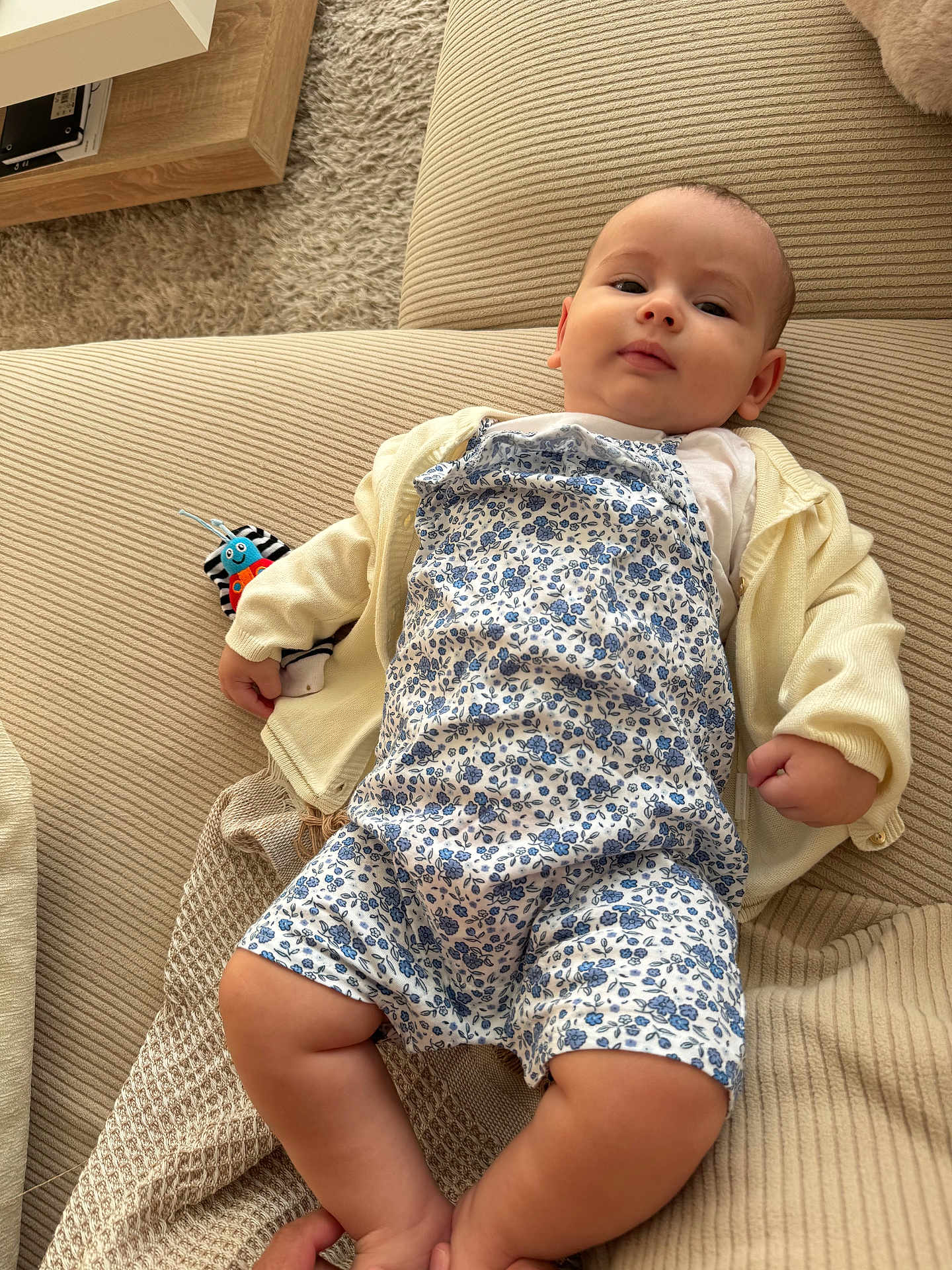 Leila participe au concours pour gagner de l'argent avec cette photo : baby, infant, child, couch, sofa, clothing, romper, cardigan, toy, striped_toy, plush_toy, beige, fabric, texture, indoor, person, relaxed, lying_down, cute, portrait