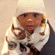 Myles joined the competition — help win amazing prizes! baby, child, hat, pom_poms, white_hat, drool, curious, cute, jacket, patterned_jacket, fluffy, indoor, carpet, sitting, portrait, warm_clothing, cozy, person, infant, closeup