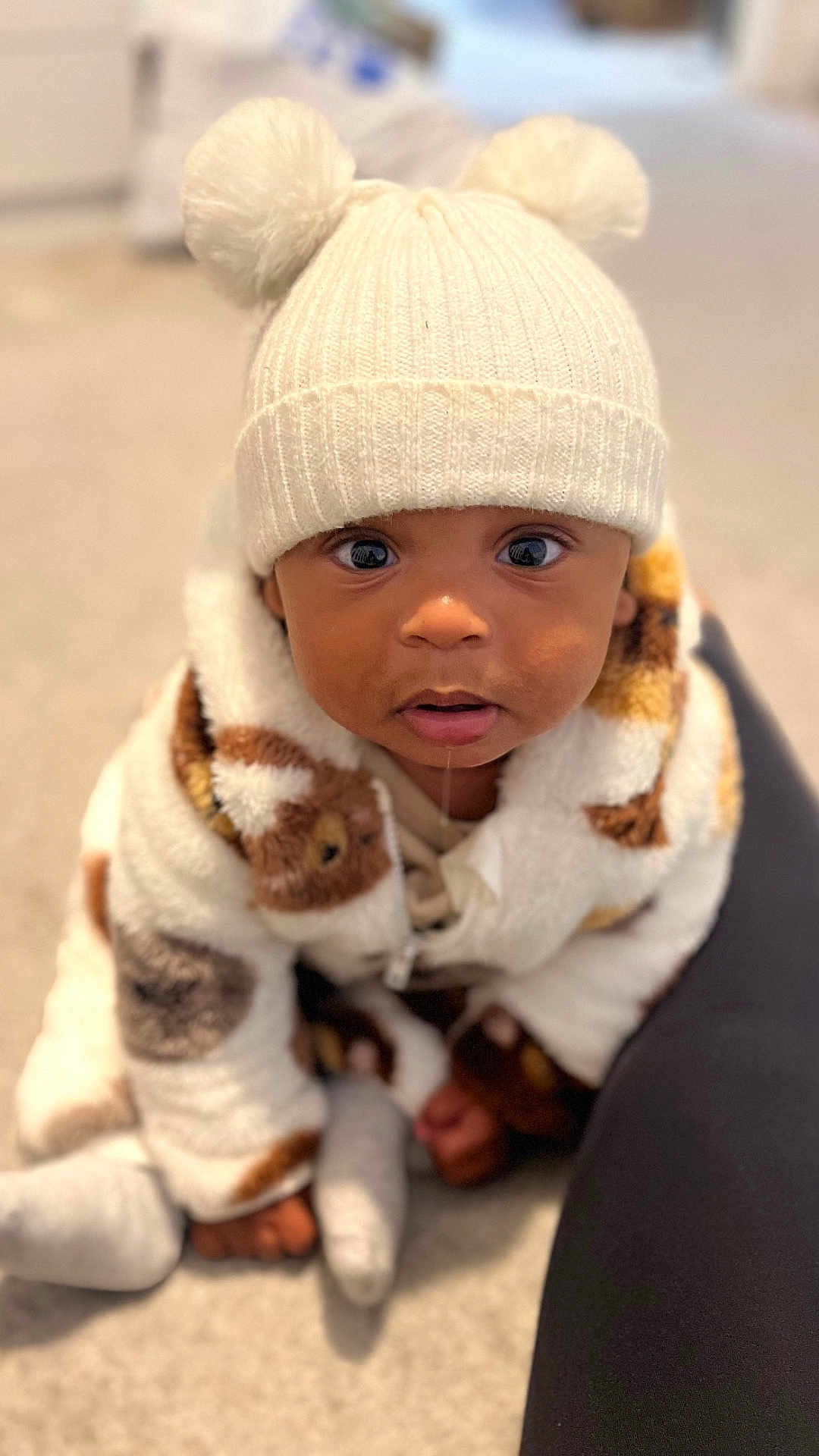 Myles joined the competition — help win amazing prizes! baby, child, hat, pom_poms, white_hat, drool, curious, cute, jacket, patterned_jacket, fluffy, indoor, carpet, sitting, portrait, warm_clothing, cozy, person, infant, closeup