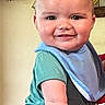 baby, child, smiling, blue_bib, green_shirt, adult_hand, indoor, face, portrait, holding, red_shirt, decor, anchor, wooden_anchor, model_ship, furniture, cute, happy, skin, person