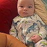 baby, infant, dinosaur_onesie, cushion, blanket, tattoo, arm, face, clothing, child, indoors, portrait, comfort, cute, person, newborn, lying_down, soft_fabric, resting, expression