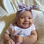 Jaleah joined the competition — help win amazing prizes! baby, infant, child, smiling, portrait, indoors, bed, bedding, lavender, headwrap, bow, onesie, clothing, sitting, lying_down, hands, face, happy, cute, photography