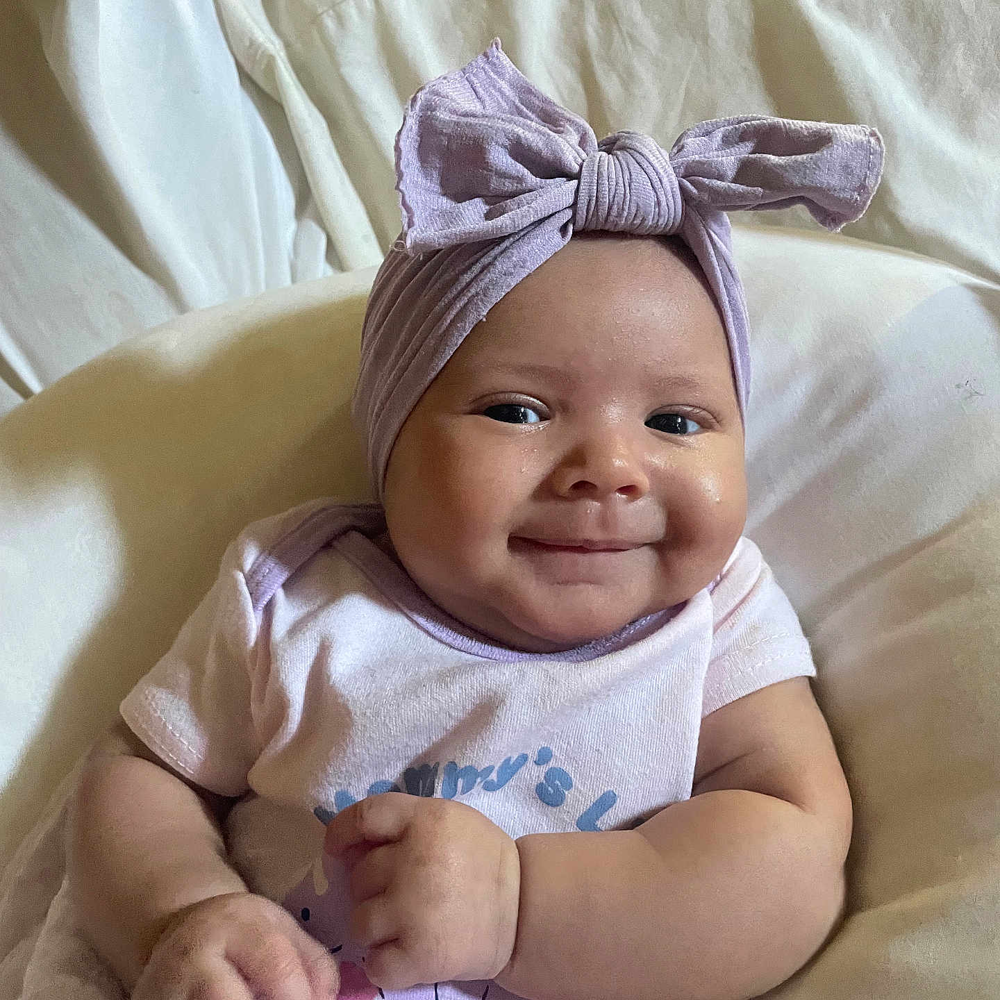 Jaleah joined the competition — help win amazing prizes! baby, infant, child, smiling, portrait, indoors, bed, bedding, lavender, headwrap, bow, onesie, clothing, sitting, lying_down, hands, face, happy, cute, photography
