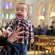 Jared- Matthew Ramos a rejoint le concours — aidez-le/la à gagner de superbes lots ! toddler, child, happy, smiling, plaid_shirt, jeans, sneakers, hands, indoor, cathedral, church, people, chairs, blurred_background, architecture, columns, lighting, portrait, person, joy