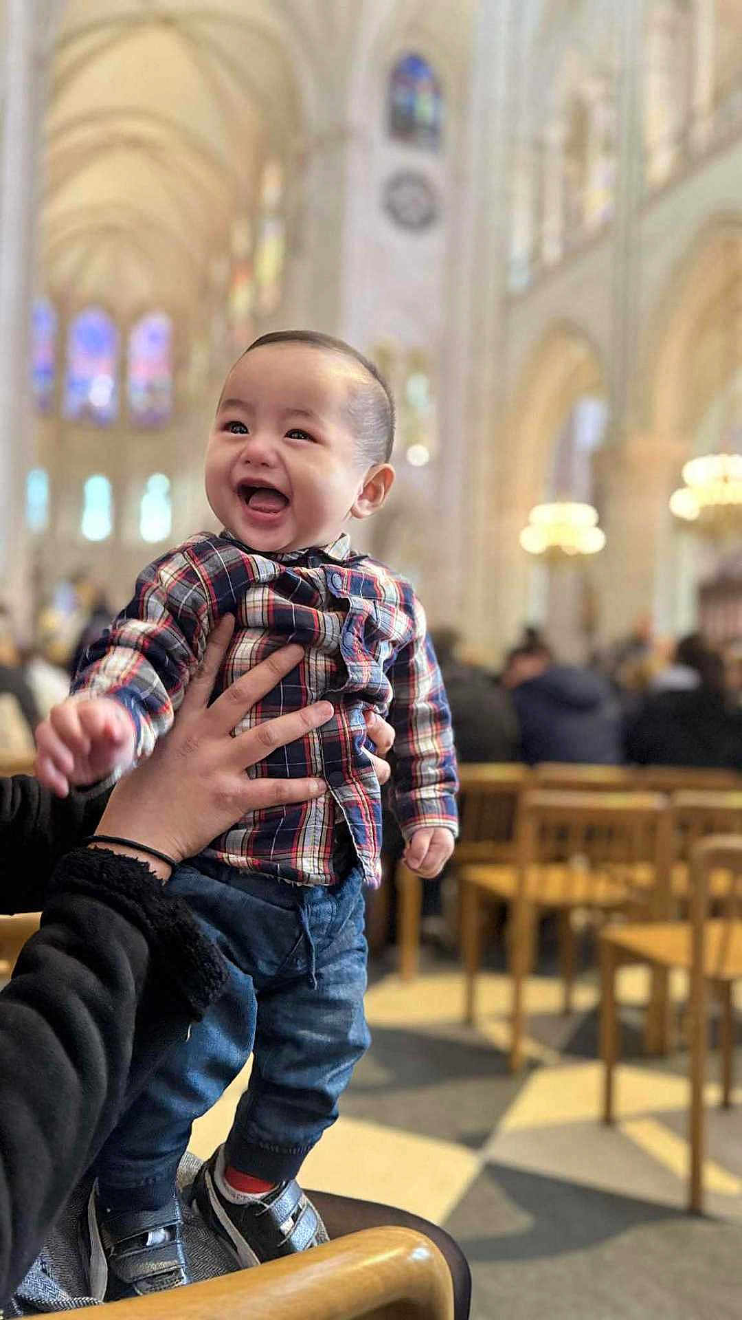 Jared- Matthew Ramos a rejoint le concours — aidez-le/la à gagner de superbes lots ! toddler, child, happy, smiling, plaid_shirt, jeans, sneakers, hands, indoor, cathedral, church, people, chairs, blurred_background, architecture, columns, lighting, portrait, person, joy