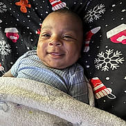 Zomani joined the competition — help win amazing prizes! baby, smile, blanket, cozy, infant, face, lying_down, festive, holiday, snowflake, gingerbread_man, mittens, clothing, cute, happy, portrait, child, indoors, soft, warm