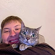 Meredith is registered to the contest to win money with this photo: person, cat, smile, face, nose_ring, tabby_cat, indoor, close_up, cuddle, pet, animal, happy, eyes, fur, clothing, portrait, head, expression, wall, texture