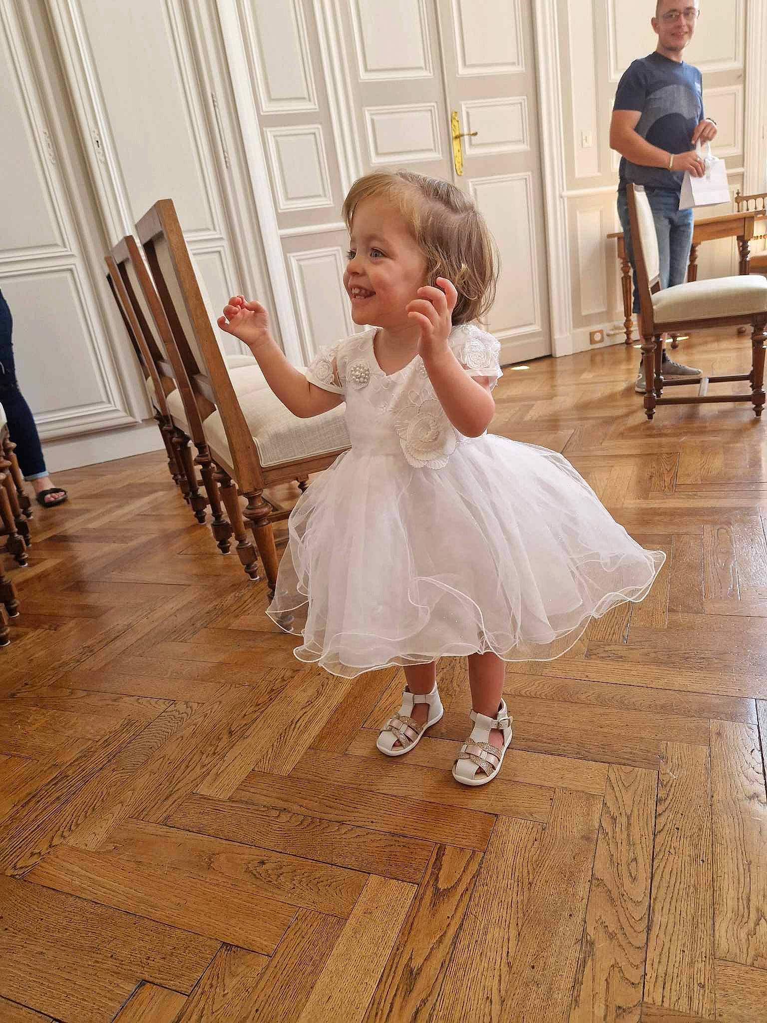 Athenais a rejoint le concours — aidez-le/la à gagner de superbes lots ! baby, baby_toddler_clothing, bridal_clothing, bridal_party_dress, chair, child, dress, event, floor, flooring, formal_wear, furniture, gown, happy, hardwood, joy, person, skin, smile, toddler