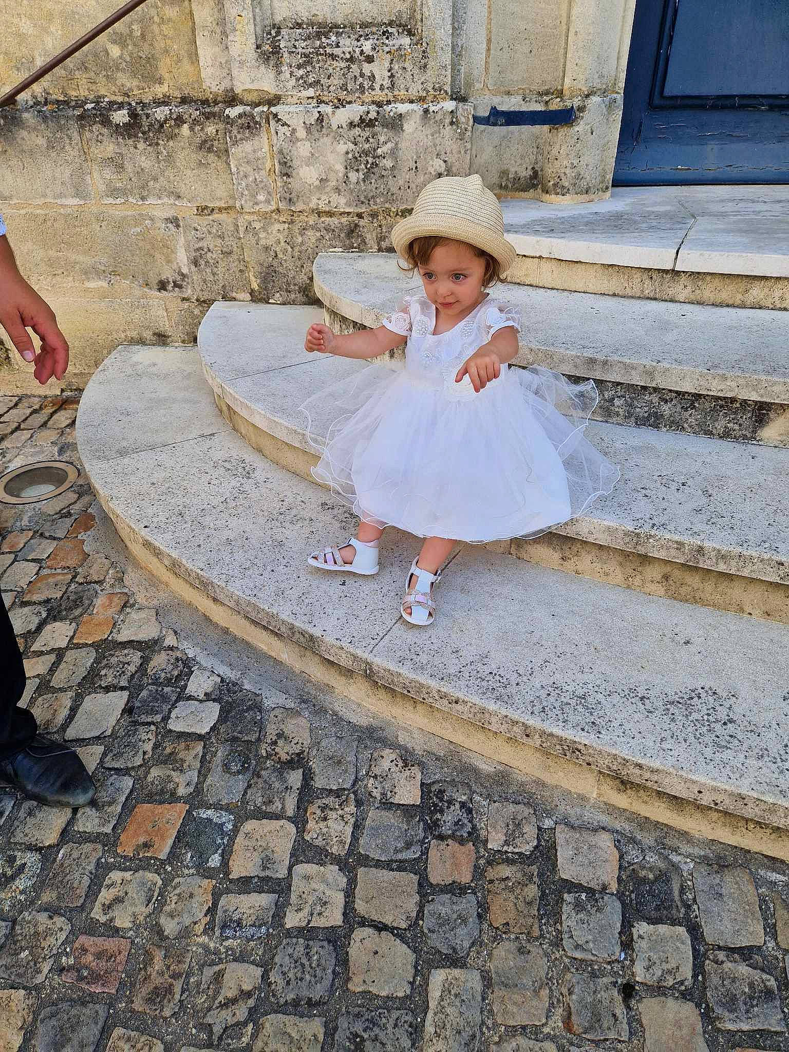 Athenais participe au concours pour gagner de l'argent avec cette photo : asphalt, child, cobblestone, dress, flooring, fun, hat, human_leg, leg, leisure, pattern, person, road, road_surface, shadow, shoe, sidewalk, sitting, standing, sun_hat