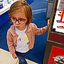 Athenais a rejoint le concours — aidez-le/la à gagner de superbes lots ! blue_carpet, casual_clothing, child, curious, display_case, elephant_shirt, glasses, hand_on_object, indoor, jeans, person, pink_jacket, red_glasses, retail, shopping, sneakers, standing, store, tile_floor, young_child