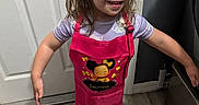Savannah joined the competition — help win amazing prizes! apron, barefoot, chef_hat, child, clothing, cute, door, flooring, girl, happy, home, indoor, kitchen, long_hair, person, playful, purple_shirt, smile, standing, wood_floor