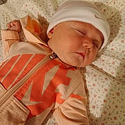 Cali is registered to the contest to win money with this photo: baby, sleeping, infant, hat, clothing, nike, zipper, hand, face, bed, sheet, floral_pattern, peaceful, cute, child, indoors, portrait, resting, soft, cozy