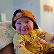 Giada joined the competition — help win amazing prizes! baby, child, smile, tongue_out, yellow_clothing, cap, backward_hat, toddler, indoor, person, cute, happy, holding, soft_light, face, young_child, onesie, patterned_clothing, casual, playful