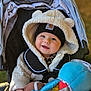 Giada is registered to the contest to win money with this photo: baby, child, stroller, jacket, hood, beanie, toy, football, plush_toy, smiling, face, hand, warm_clothing, outdoor, happy, person, infant, cute, seat_belt, closeup