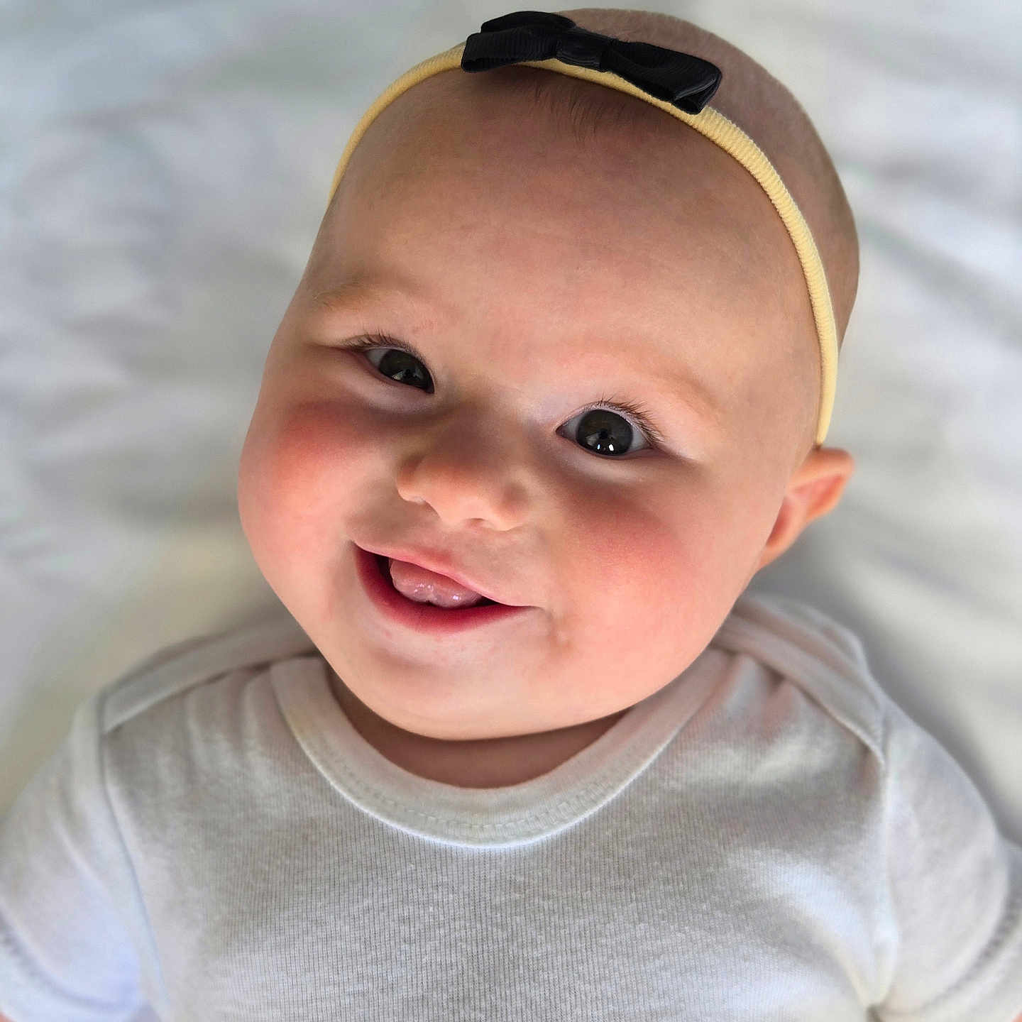 Giada joined the competition — help win amazing prizes! baby, background, cheeks, child, closeup, cute, expression, eyes, face, happy, headband, infant, lying_down, mouth, portrait, skin, smiling, soft_light, tongue, white_onesie