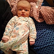 Liliana joined the competition — help win amazing prizes! baby, infant, onesie, floral_pattern, blanket, bed, blue_sheet, pink_blanket, face, person, newborn, clothing, sleepwear, fist, expression, indoor, cute, young_child, lying_down, soft_texture