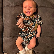 Crue joined the competition — help win amazing prizes! baby, smiling, camo_onesie, white_socks, couch, gray_furniture, infant, happy, reaching_hand, indoor, person, child, cute, plush, seated, young_baby, cozy, portrait, casual_clothing, relaxed