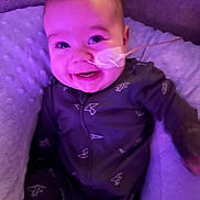 Jackson is registered to the contest to win money with this photo: baby, infant, smiling, face, nasal_tube, medical, onesie, paper_airplane_pattern, purple_light, cushion, soft_texture, seated, child, cozy, happy, indoors, portrait, cute, healthcare, person