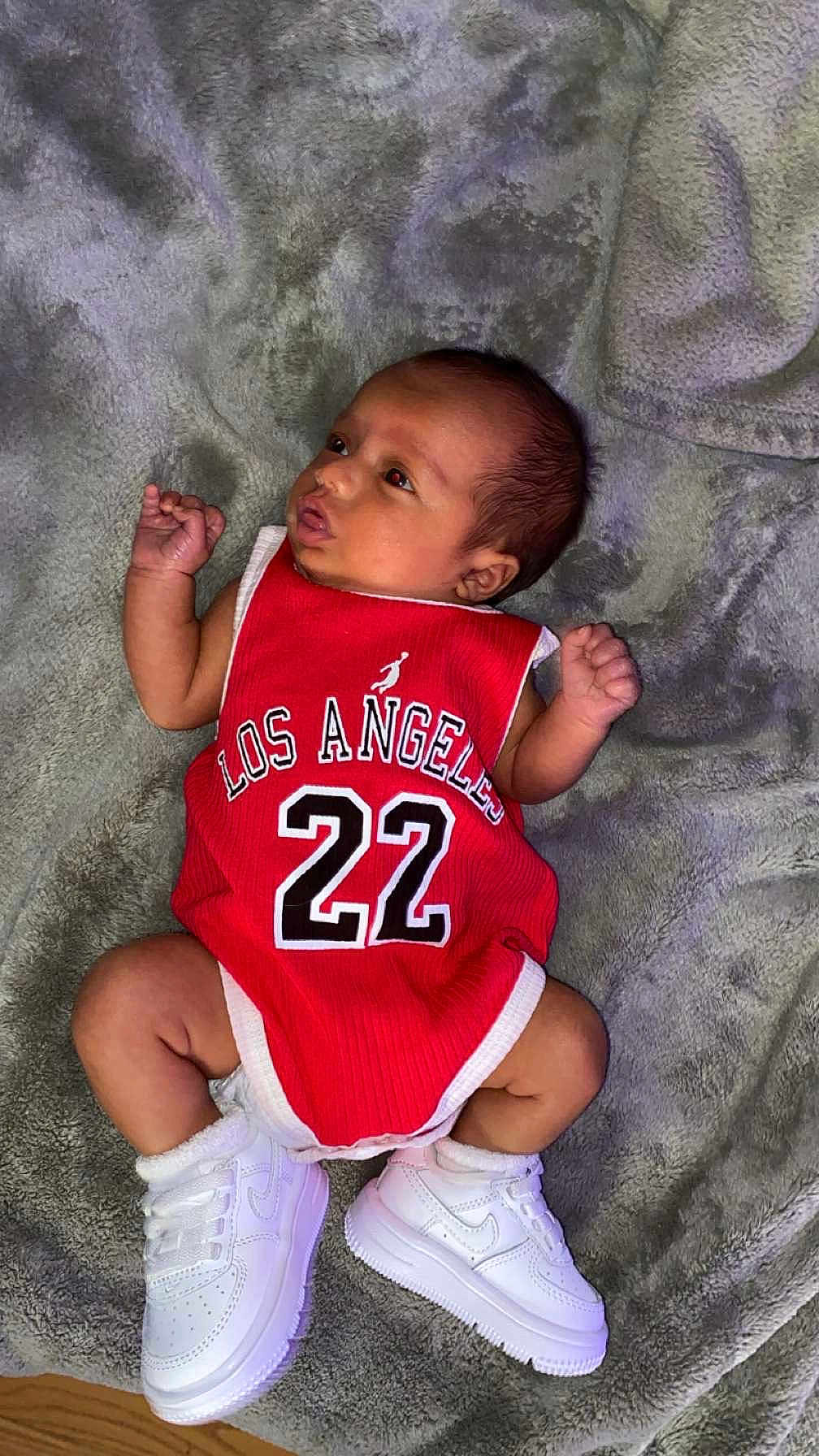 Mateo is registered to the contest to win money with this photo: baby, blanket, casual, child, clothing, cute, footwear, indoor, infant, los_angeles, lying_down, newborn, number_22, person, portrait, red_jersey, small_feet, small_hands, soft_texture, white_sneakers
