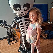 Raven joined the competition — help win amazing prizes! child, girl, curly_hair, barefoot, inflatable, skeleton, balloon, indoor, wooden_floor, tv, furniture, smile, casual_clothing, playful, decor, living_room, toy, happy, person, home