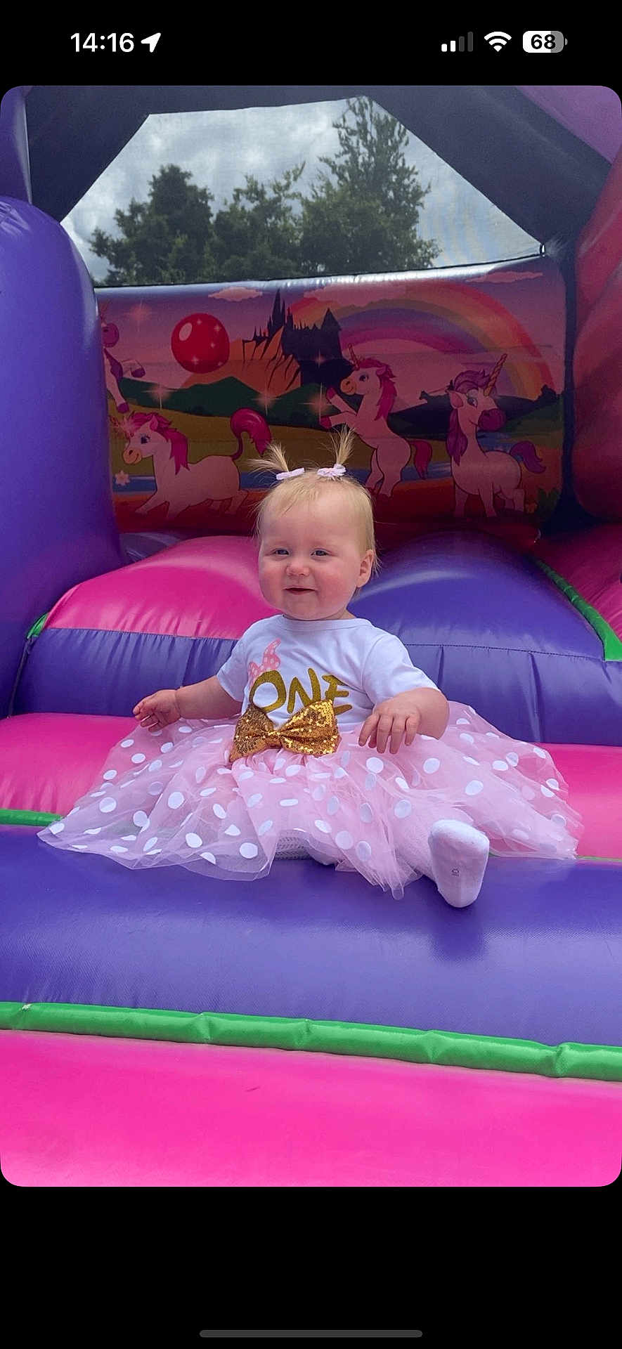 Sierra is registered to the contest to win money with this photo: baby, child, infant, toddler, birthday, party, dress, tutu, bow, pigtails, inflatable, bouncy_castle, unicorn, rainbow, outdoor, sky, cloud, grass, pink, purple