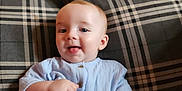 Alex is registered to the contest to win money with this photo: baby, child, blue_clothing, couch, plaid, smiling, tongue_out, indoor, seated, cute, infant, happy, person, young_child, soft_light, home, furniture, portrait, skin, face