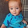 Alex is registered to the contest to win money with this photo: baby, child, blue_clothing, polka_dot, couch, cushion, face, eyes, hand, indoor, infant, person, portrait, seated, skin, sitting, small_child, toddler, young_child, orange_wall