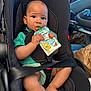 baby, black_car_seat, car_interior, car_seat, child, child_safety, clothing, cute, feet, food_pouch, green_shirt, hands, infant, legs, natural_light, portrait, seatbelt, sitting, toy_ball, vehicle