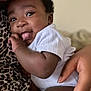 Zahrah joined the competition — help win amazing prizes! baby, infant, child, onesie, hand, curly_hair, tongue_out, close_up, face, skin, person, cute, playful, expression, soft_light, indoor, holding, comfort, leopard_print, smile