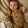 baby, infant, blanket, brown_outfit, hearts_pattern, cute, lying_down, soft_texture, indoors, portrait, child, small_hand, face, eyes, cozy, warm_colors, sleepwear, newborn, resting, comfortable
