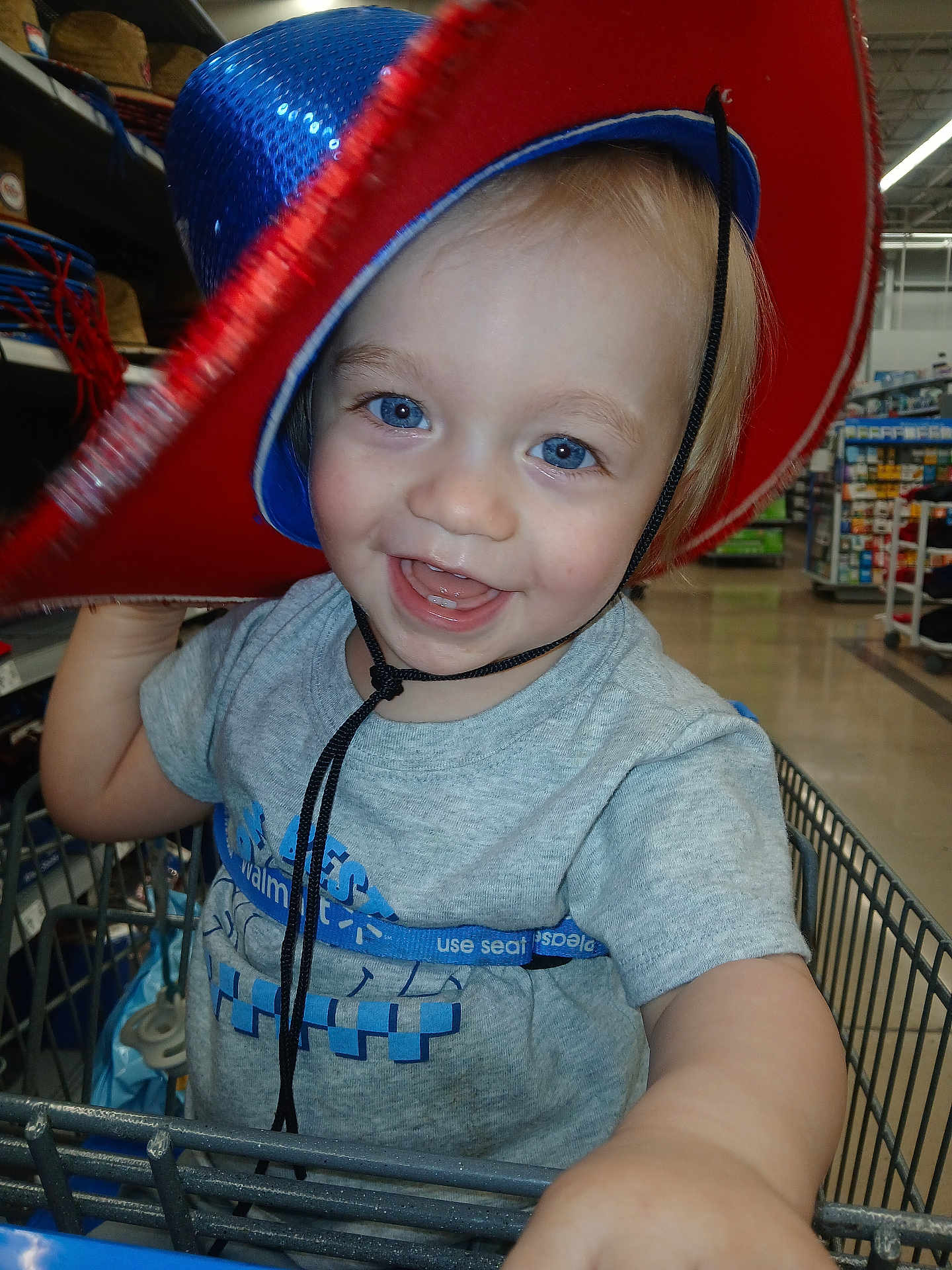 Declan joined the competition — help win amazing prizes! child, toddler, smiling, blue_eyes, cowboy_hat, shopping_cart, store, aisle, clothing, short_sleeve_shirt, happy, person, retail, indoor, baby, cute, face, hat, playing, closeup