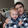 Declan is registered to the contest to win money with this photo: baby, child, sibling, hug, smile, plaid_shirt, blue_eyes, indoor, table, chair, person, face, young, caucasian, happy, casual_clothing, mustache, short_hair, light_skin, family