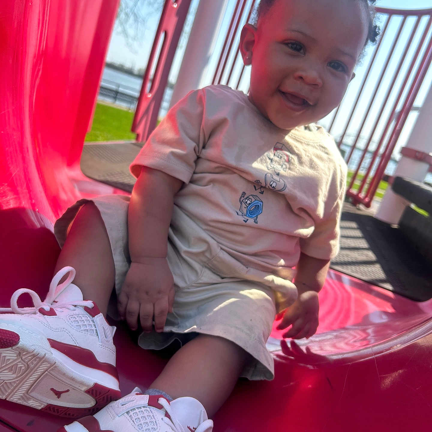 Dakari joined the competition — help win amazing prizes! toddler, child, slide, playground, outdoor, smiling, sneakers, red, beige_clothing, hair_puffs, sunny, grass, happy, park, daylight, young_child, casual_wear, play, fun, cute