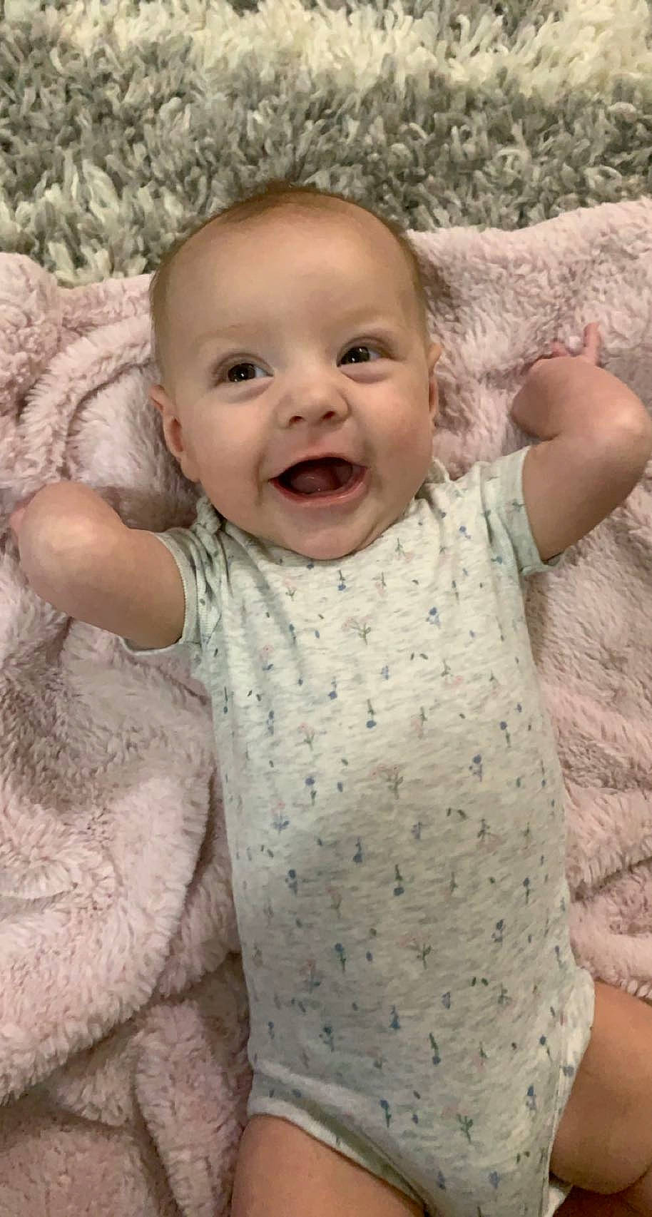 Lucia is registered to the contest to win money with this photo: arm, baby_toddler_clothing, cheek, eye, face, facial_expression, gesture, hand, head, iris, lip, neck, nose, organ, outerwear, person, skin, sleeve, smile, standing