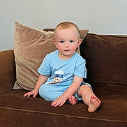 James is registered to the contest to win money with this photo: toddler, child, baby, couch, sofa, pillow, blue_clothing, sitting, indoor, face, barefoot, cute, young_child, person, home, furniture, portrait, casual, relaxed, cozy
