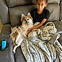 child, dog, couch, blanket, smiling_dog, happy, indoor, furniture, leopard_print, phone_case, braided_hair, black_shirt, pet, cozy, relaxed, lying_down, human, home, tongue_out, cup_holder